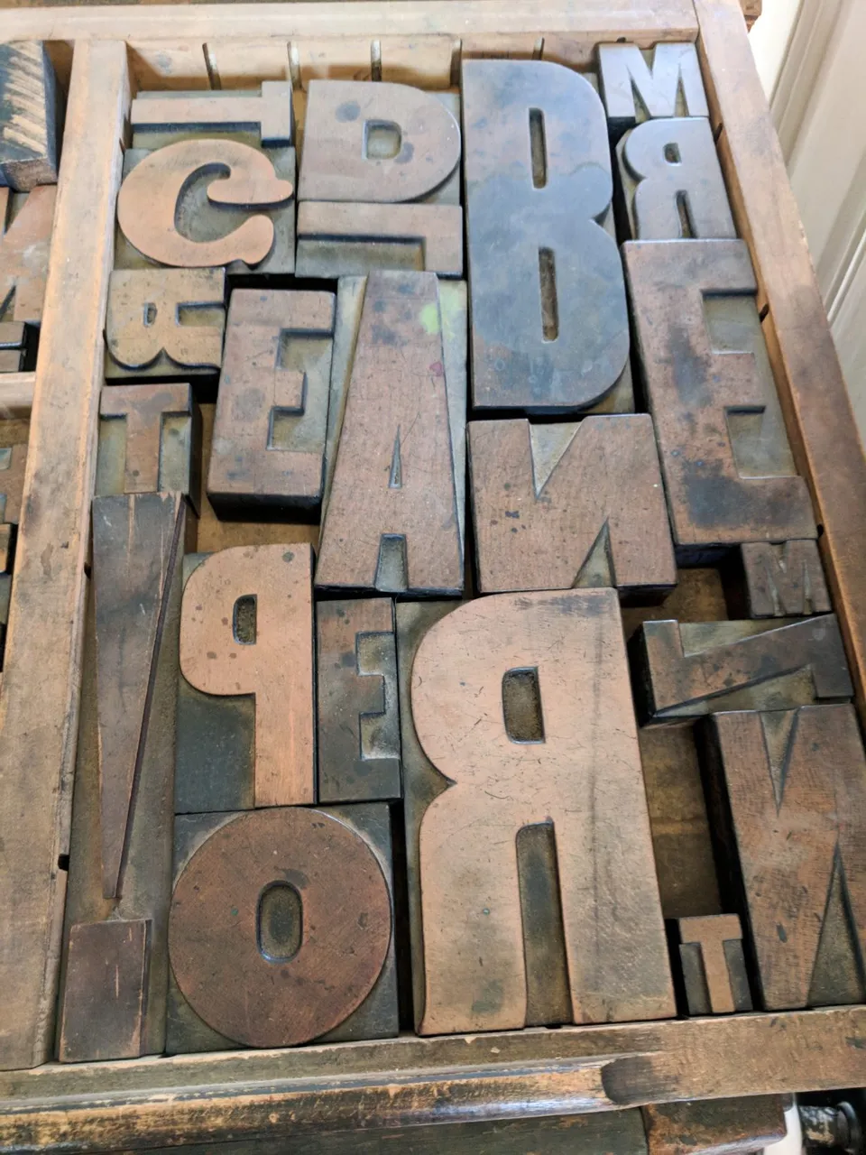 Worn wooden printing letters fill a shallow tray.