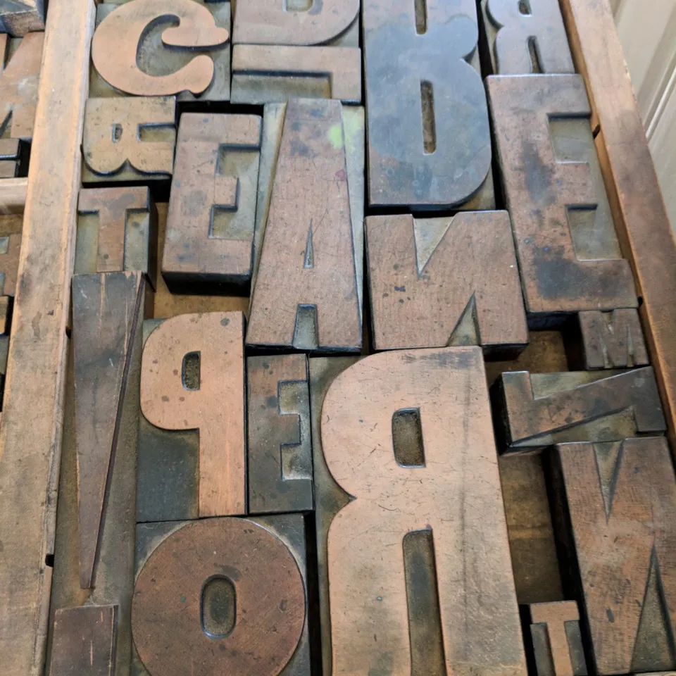Worn wooden printing letters fill a shallow tray.