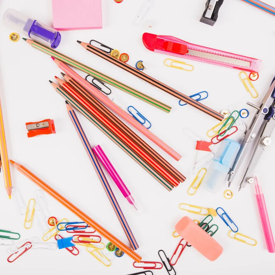 Bright pencils, pens, paper clips, a compass and rulers lie on a white surface.