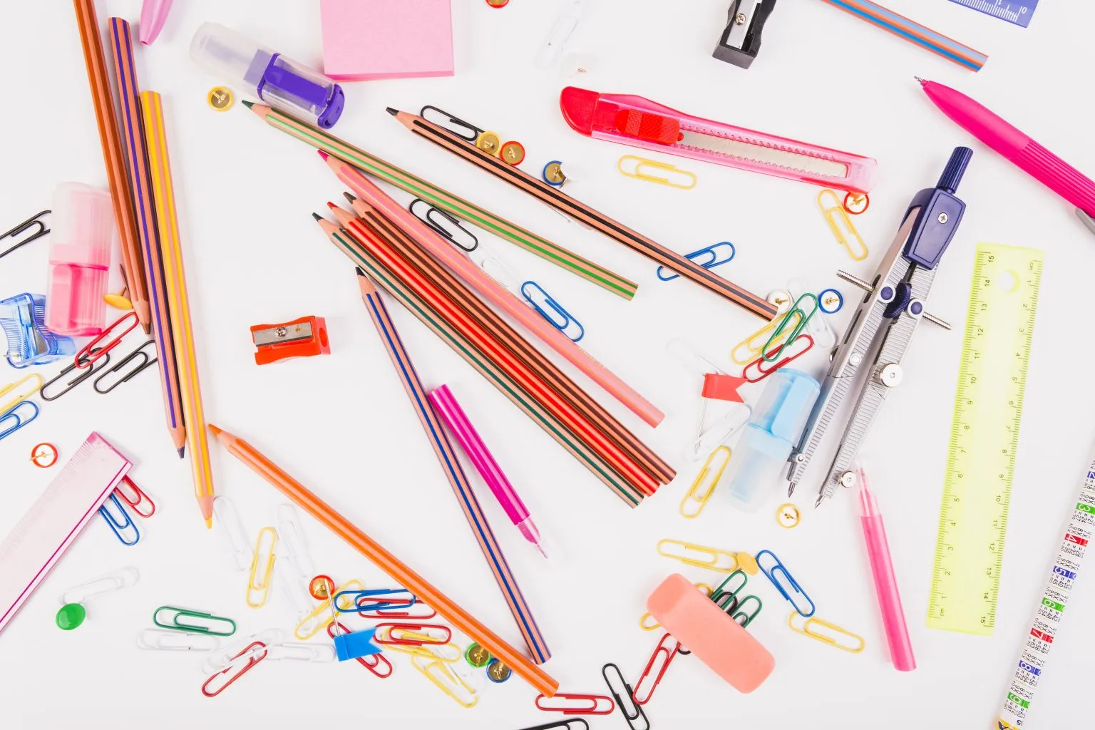 Bright pencils, pens, paper clips, a compass and rulers lie on a white surface.