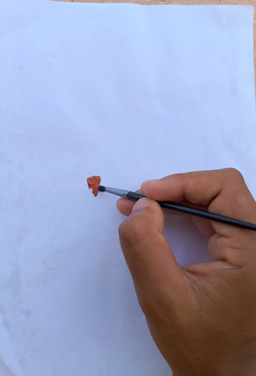 A hand holds a brush making a small red stroke on white paper.