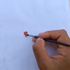 A hand holds a brush making a small red stroke on white paper.